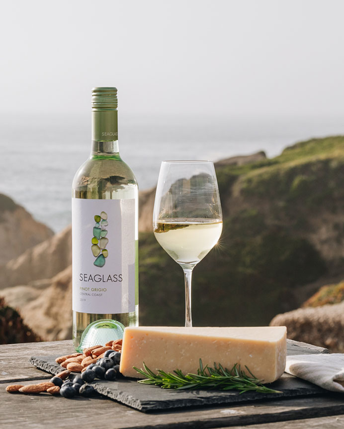 Bottle of Seaglass Central Coast Pinot Grigio white wine with cheese on an outdoor table with a scenic background